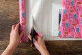 WomanÃ¢â¬â¢s hands cutting pink wrapping paper to wrap a calendar, wood table